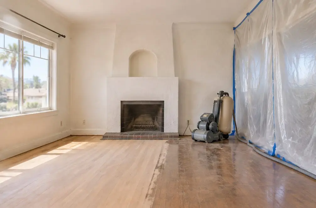 Illustration: a west-side Chula Vista, CA bungalow living room with a sanded oak floor half covered in a first coat of finish, a drum sander parked by the wall and the room closed off with plastic sheeting